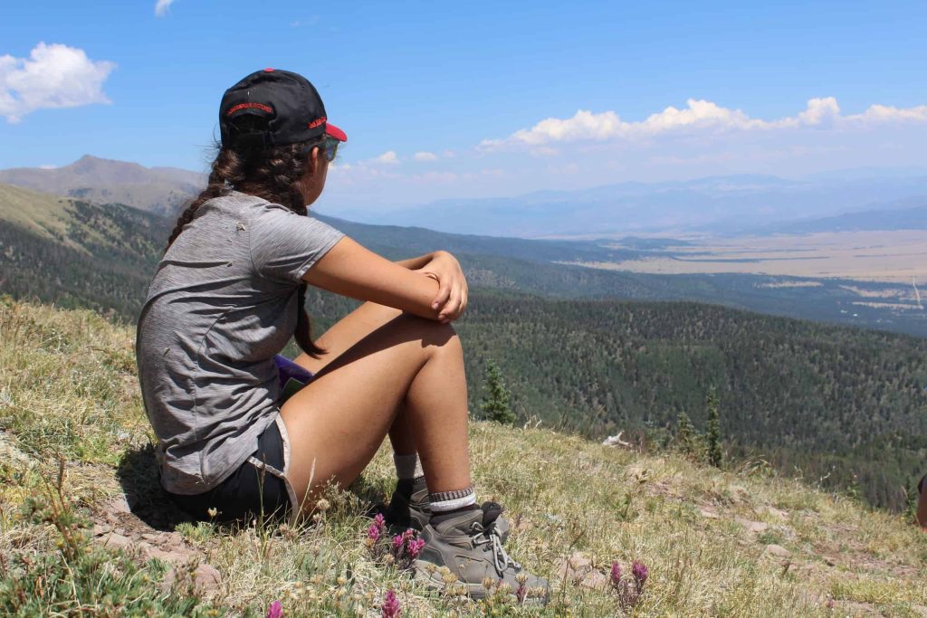 A girl sits on a hill with a view. Her back is towards the camera.